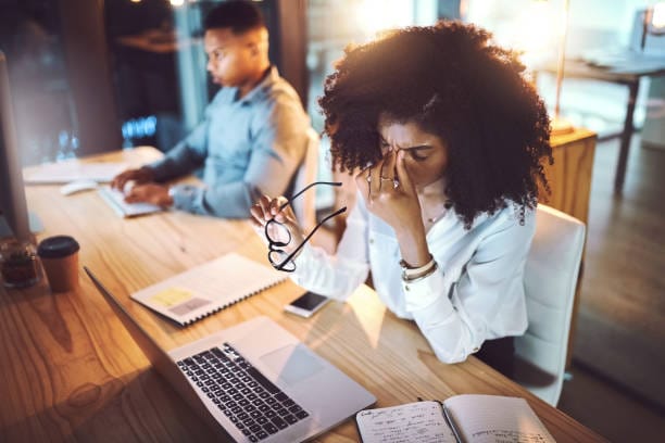 Shot of a young businesswoman rubbing her eyes while working alongside her colleague in an office at night