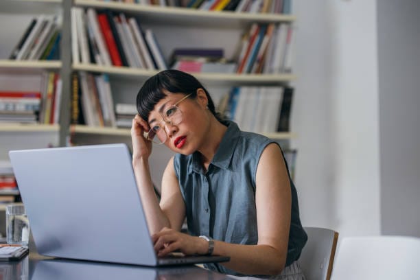 An upset Japanese entrepreneur reading something on her laptop while missing some deadline.  She is sitting at her office desk.