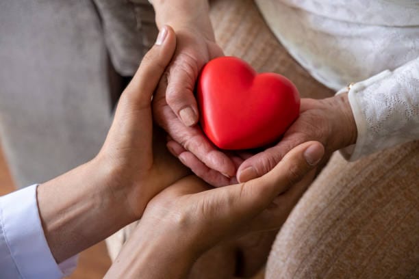 Taking care for the elderly concept with a wrinkled hands and young hands holding a red heart shape