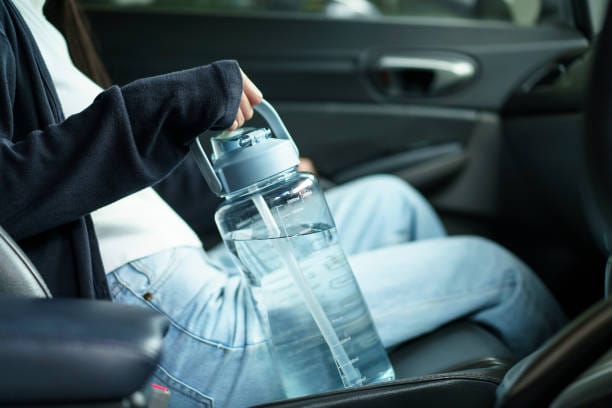 Asian young woman holding a reusable plastic bottle when traveling by the car, woman preparing a drinking water in reusable plastic bottle.