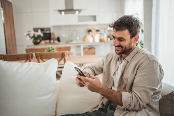 Portrait of cheerful man using smart phone at home living room