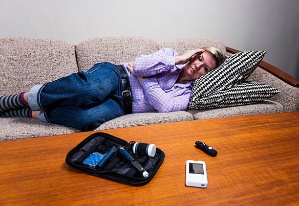 A middle-aged diabetic woman suffering from a glucose crash, also known as a diabetes sugar crash or hypoglycaemia lying on a couch at home..