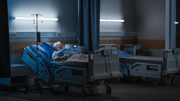 Hospital Ward: Portrait of Elderly Man Wearing Oxygen Mask Resting in Bed, Struggling to Recover after Covid-19, Sickness, Disease, Surgery. Old Man Fighting for His Life. Dark Blue Tragic Shot