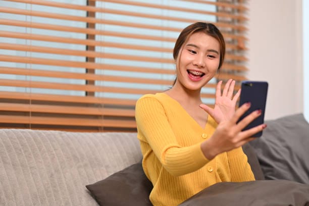 Cheerful teenage asian girl having video call joyfully on her smartphone at home.